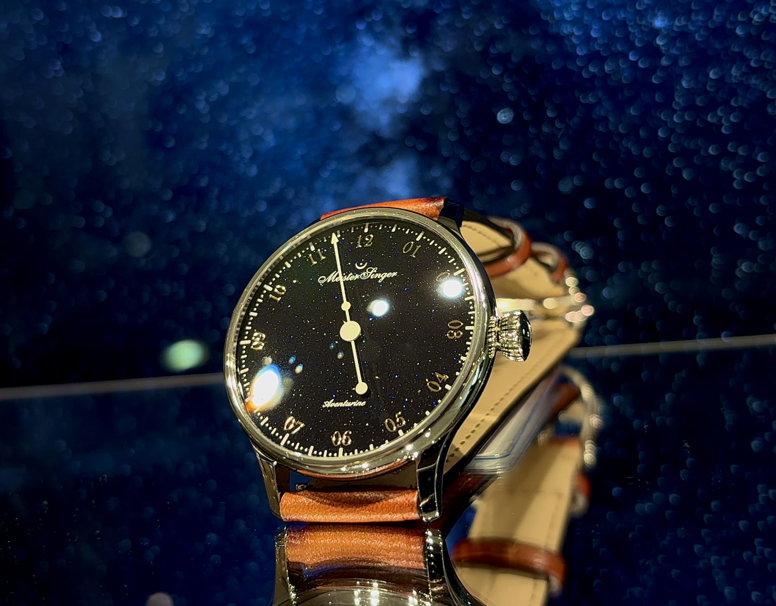 MeisterSinger（マイスタージンガー） Pangaea Aventurine パンゲア アベンチュリン。ゴールドインデックスとクラシカルなフォントが輝くブルーアベンチュリンダイヤル。シングルハンドのデザインが素材本来の煌めきを最大限に引き立て、裏面からはスイス製ムーブメントSellita SW200の精緻な動きを鑑賞可能。美しさと機能性を兼ね備えた一本針の機械式腕時計。