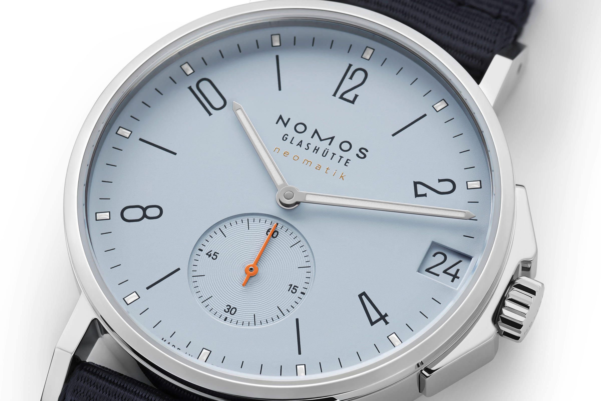 NOMOS Glashütte / Ahoi neomatik 38 Date Sky / NM526　20気圧の防水性能を持つスポーツウォッチ「アホイ」の新作、「アホイ・ネオマティックデイト38 スカイ＆サンド」。  新しいアホイはデイト機能付きネオマティックを搭載しながら直径わずか38.5 ミリ、ケースの厚みは9.9 ミリ。 スポーツウォッチを最もエレガントにした逸品となりました。  両面に無色の反射防止コーティングを施したサファイアクリスタルを通してみる文字盤は、澄み切った青空のスカイブルーと輝く黄金色のサンドカラー。 インデックス、針、分メモリのポイントにはスーパールミノバが塗布され暗闇での視認性を確保します。 テキスタイルストラップは、フランスから取り寄せたテーラーメイド。 スタイルにこだわる全ての要素を満たします。  日中も夜も同じように正確でパワフル、完璧なプロポーション。 驚くほど薄型で、手首に自然と落ち着きます。 オフィスでも水中でも、夕暮れを楽しむひとときにも、あらゆる場面にふさわしいスポーティな自動巻き腕時計です。 ねじ込み式のリューズだけでなくリューズガードを配することで水周りでも安心