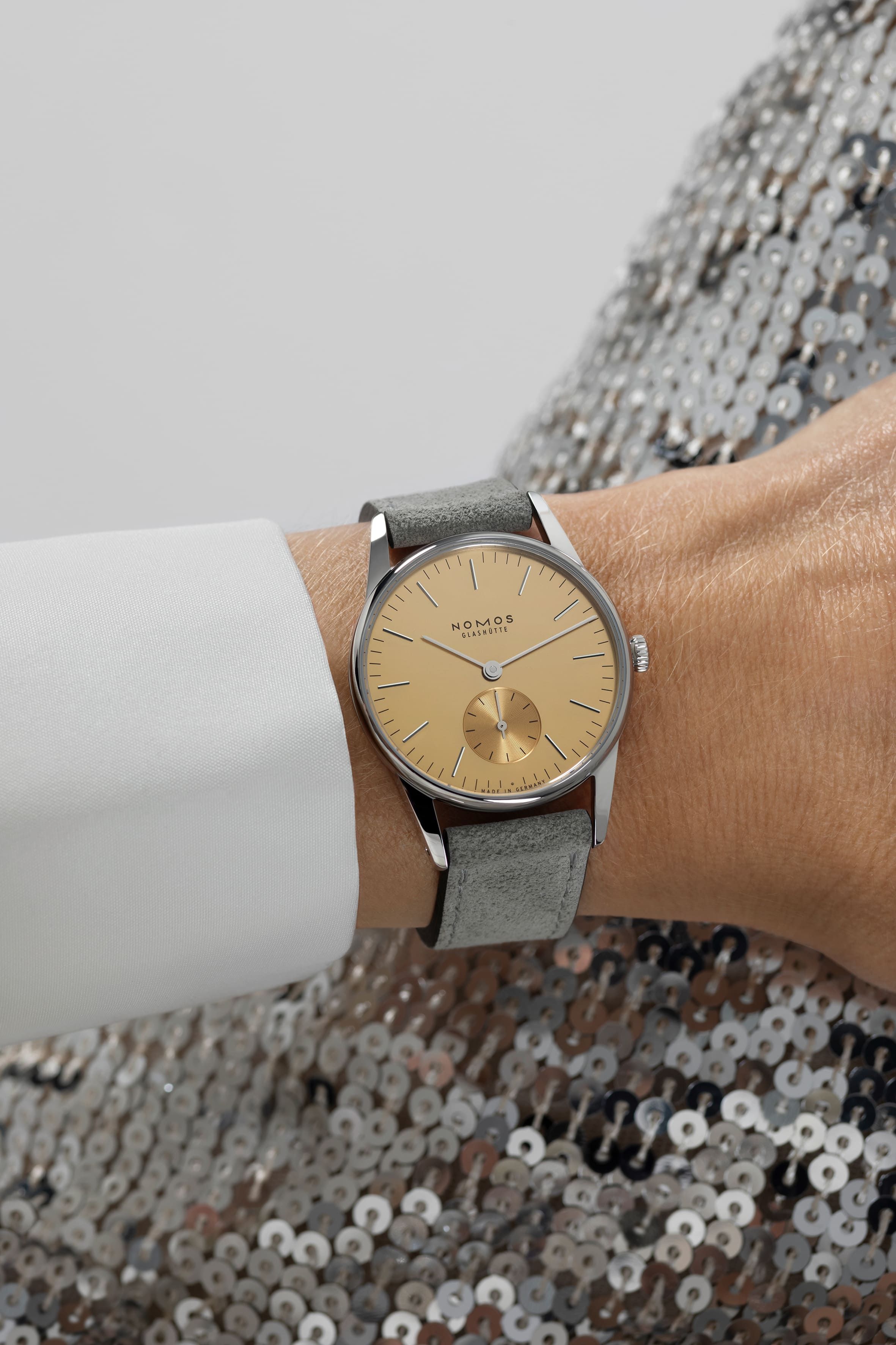 NOMOS Glashütte / ORION33/ OR1A3SG233　359ノモス グラスヒュッテのクラシックモデルの一つであるオリオンから、ギフトに最適な新作です。 オリオン 33 ゴールドとオリオン 38 シルバーは、特別な価値を持っています。 それは華やかだった「黄金の 1920 年代」を思い起こさせます。 オリオンはグラスヒュッテ伝統のデザインに回帰しました。 近年のミニマルデザインではなく、グラスヒュッテの時計学校でウオッチメーカーたちが製作していたデザインです。 銀色のケースに手作業で植えこんだインデックスをもつ文字盤です。 サイズは2 つあり、小さいサイズは誇らしげなサーモンゴールド、一方大きい方はシルバーの文字盤にゴールドカラーのインデックスで、 いずれも男女問わず着けることが出来ます。 亜鉛メッキにゴールドまたはシルバーのポリッシュ仕上げがされた文字盤にはファセット状のアプライドインデックス（植え字）がセットされています。 通常ラインのモデルよりも手間をかけた、 1 クラス上級なオリオンなのです。 ライトなカラーのベロアレザーストップが、アクセントとしてウォッチに注目を集めます。特にデ
